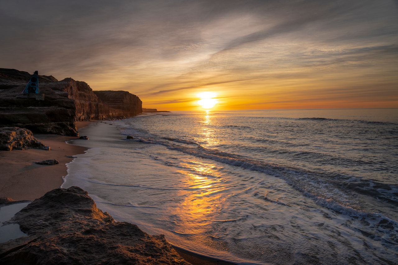Steep coastal cliff with waves crashing at sunrise