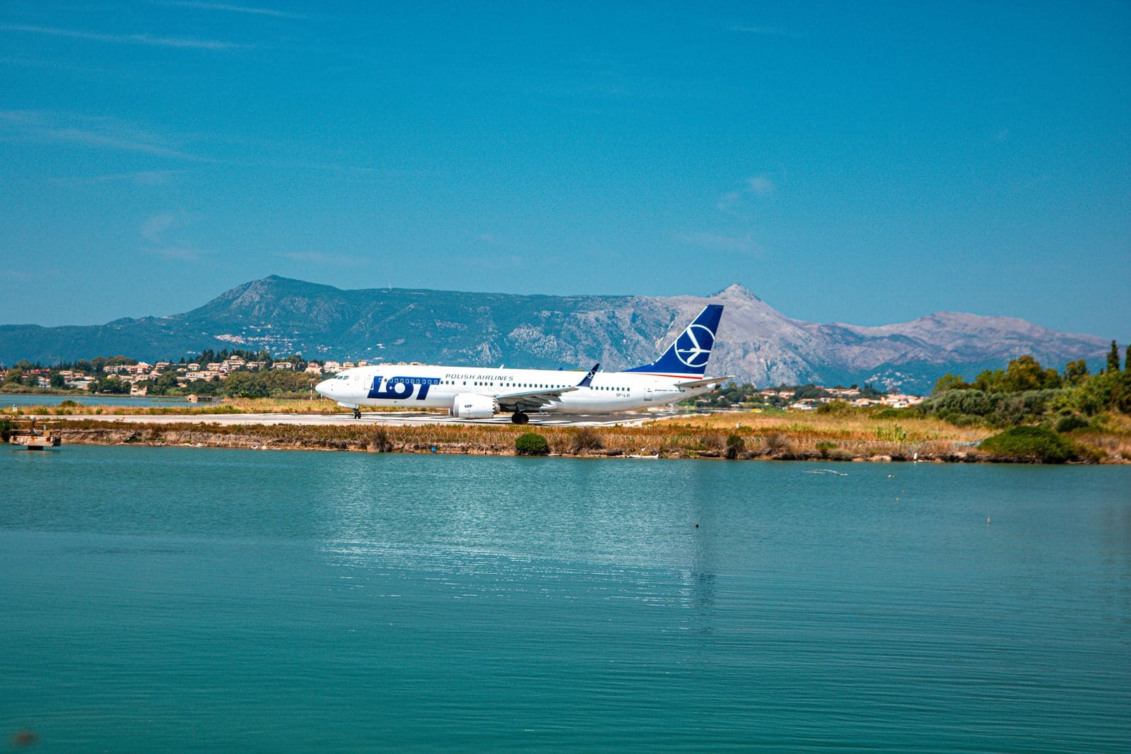 A short paved runway cutting across a flat tropical island with palm trees nearby