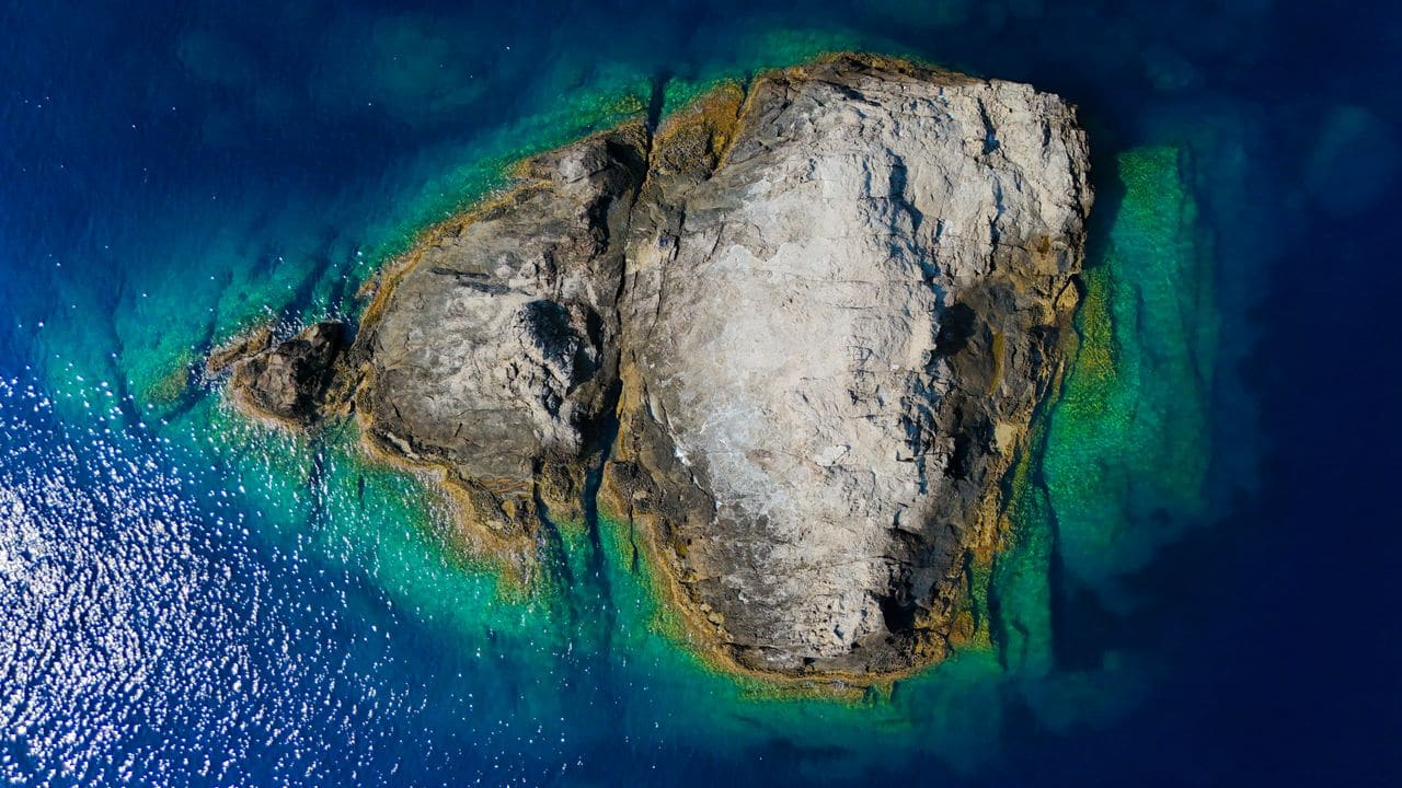 Aerial view of a tropical island showing a rugged shoreline and clear water