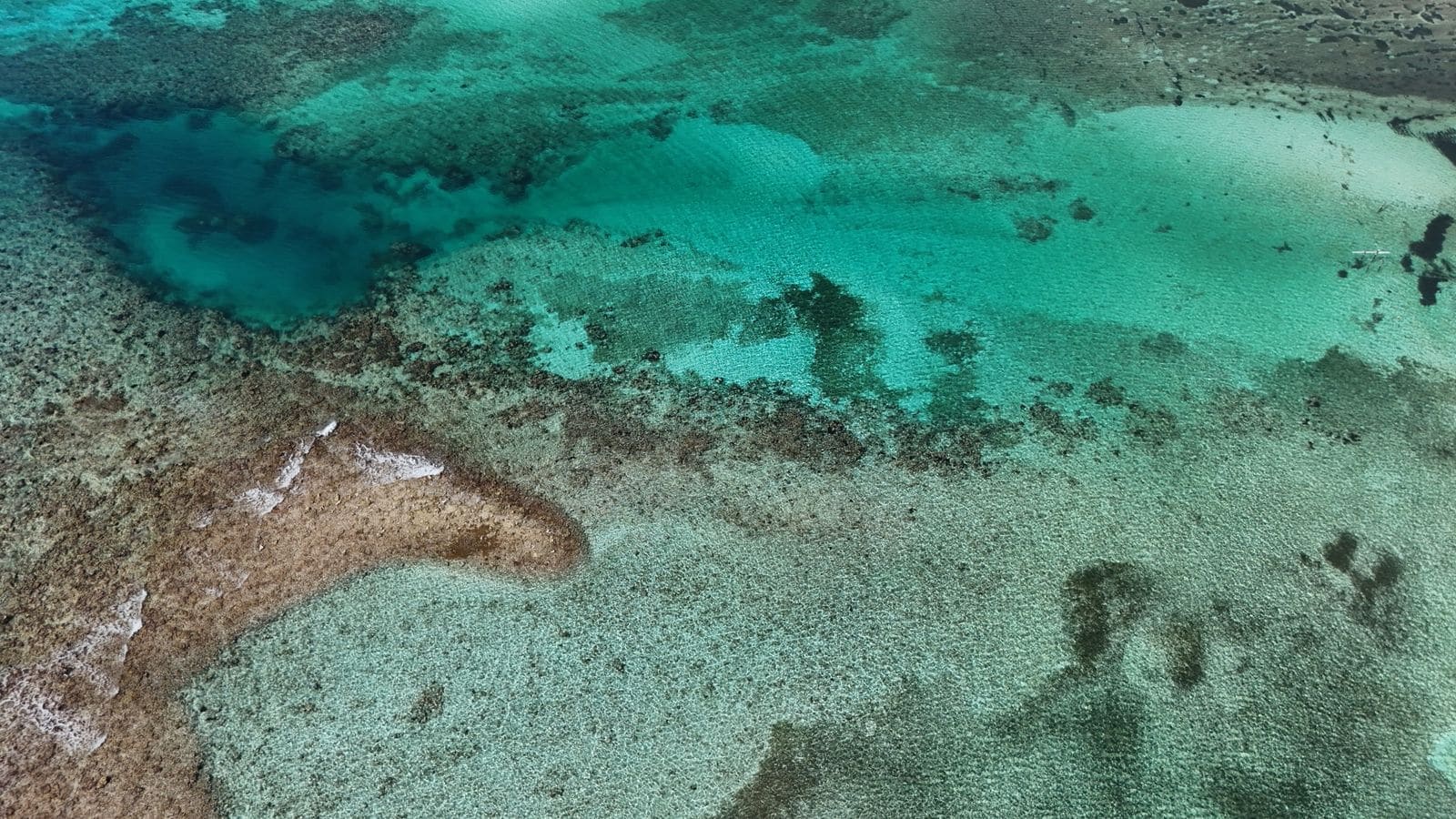 Turquoise water flowing over a coral reef beneath steep island cliffs