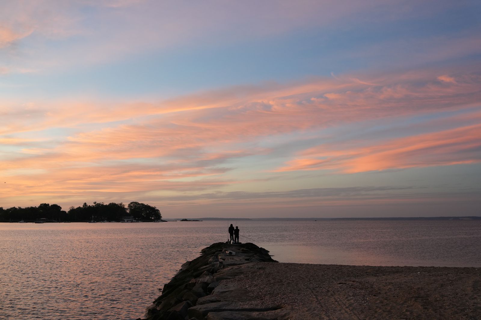 A wooden jetty extending into calm sea at sunrise with gentle light